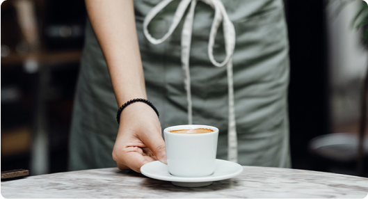 Barista serving a cup of coffee in white ceramic mug